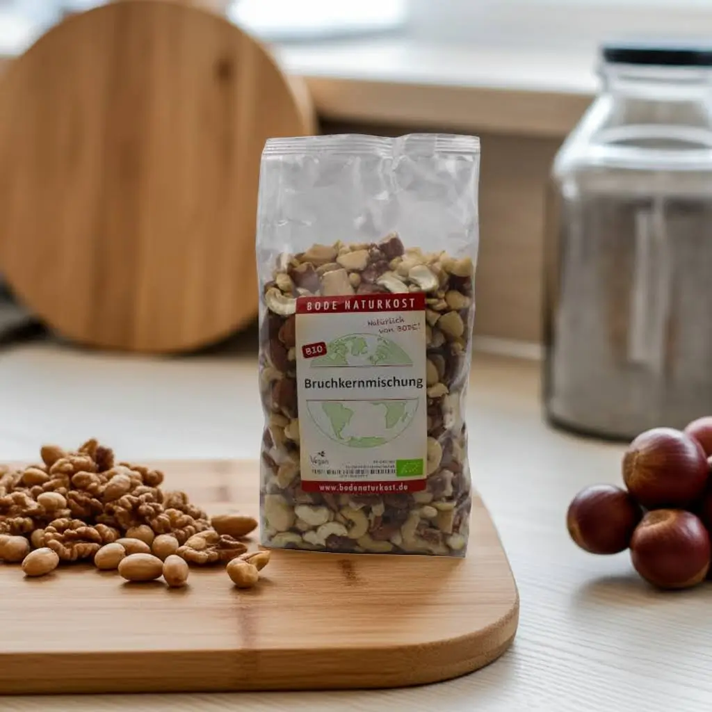 A bag of broken mixed nuts stands in a kitchen on a board, kitchen utensils in the background
