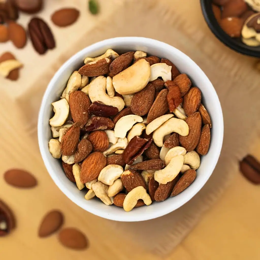Nut mix in a bowl on a wooden table, with a few nuts lying beside it