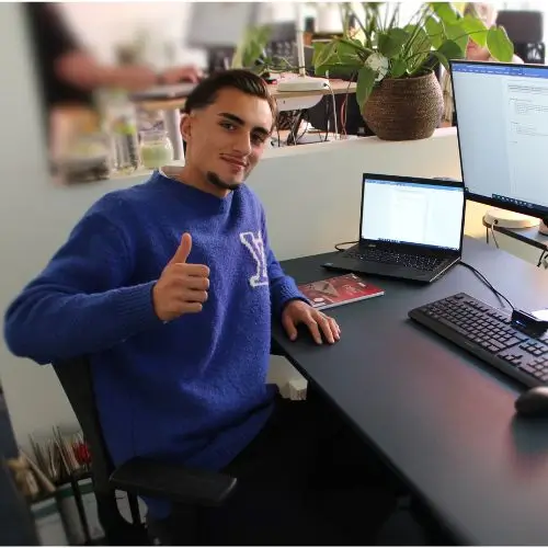 Apprentice Diyar at a desk, looking friendly and giving a thumbs-up.