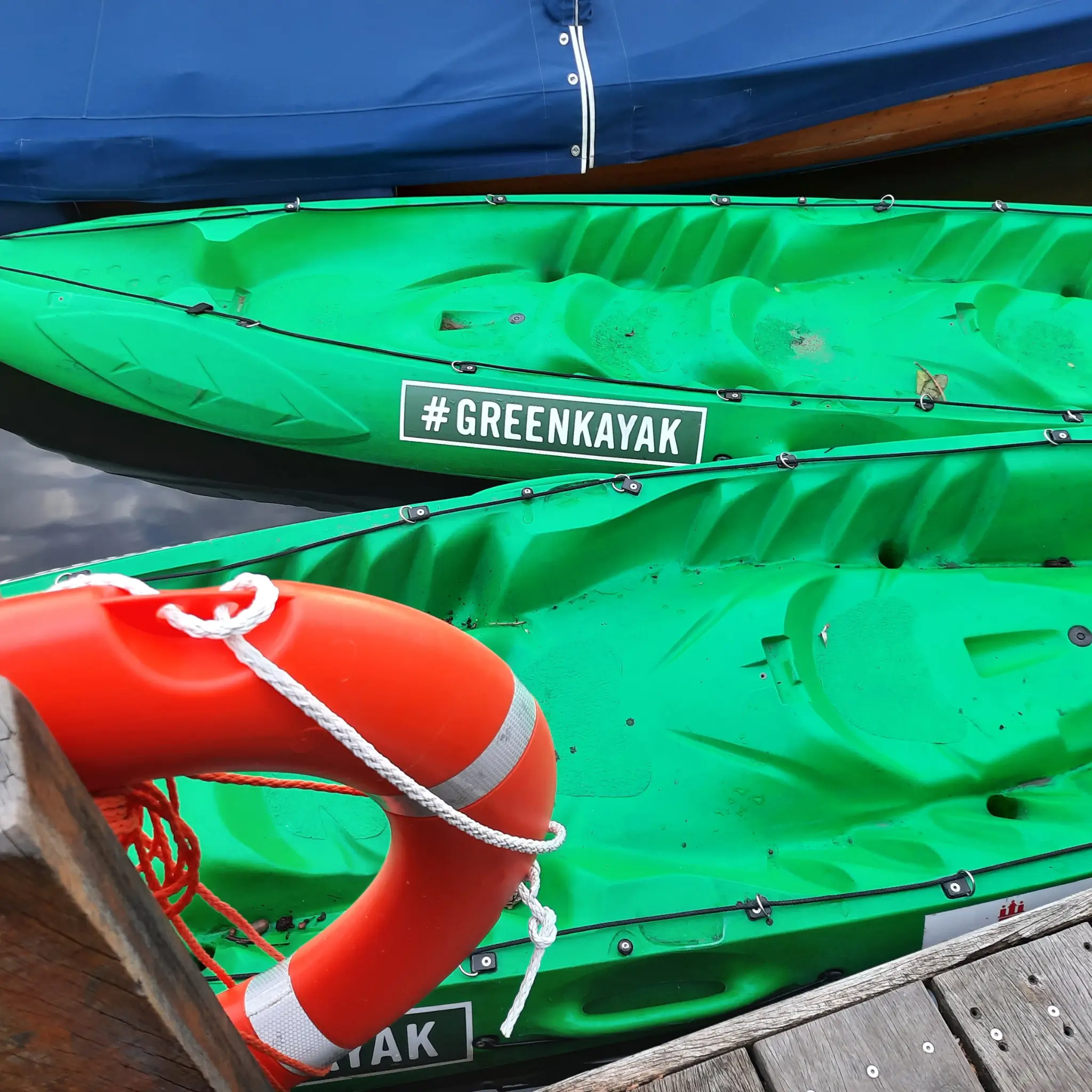 Two green kayaks in the water, life ring on the jetty