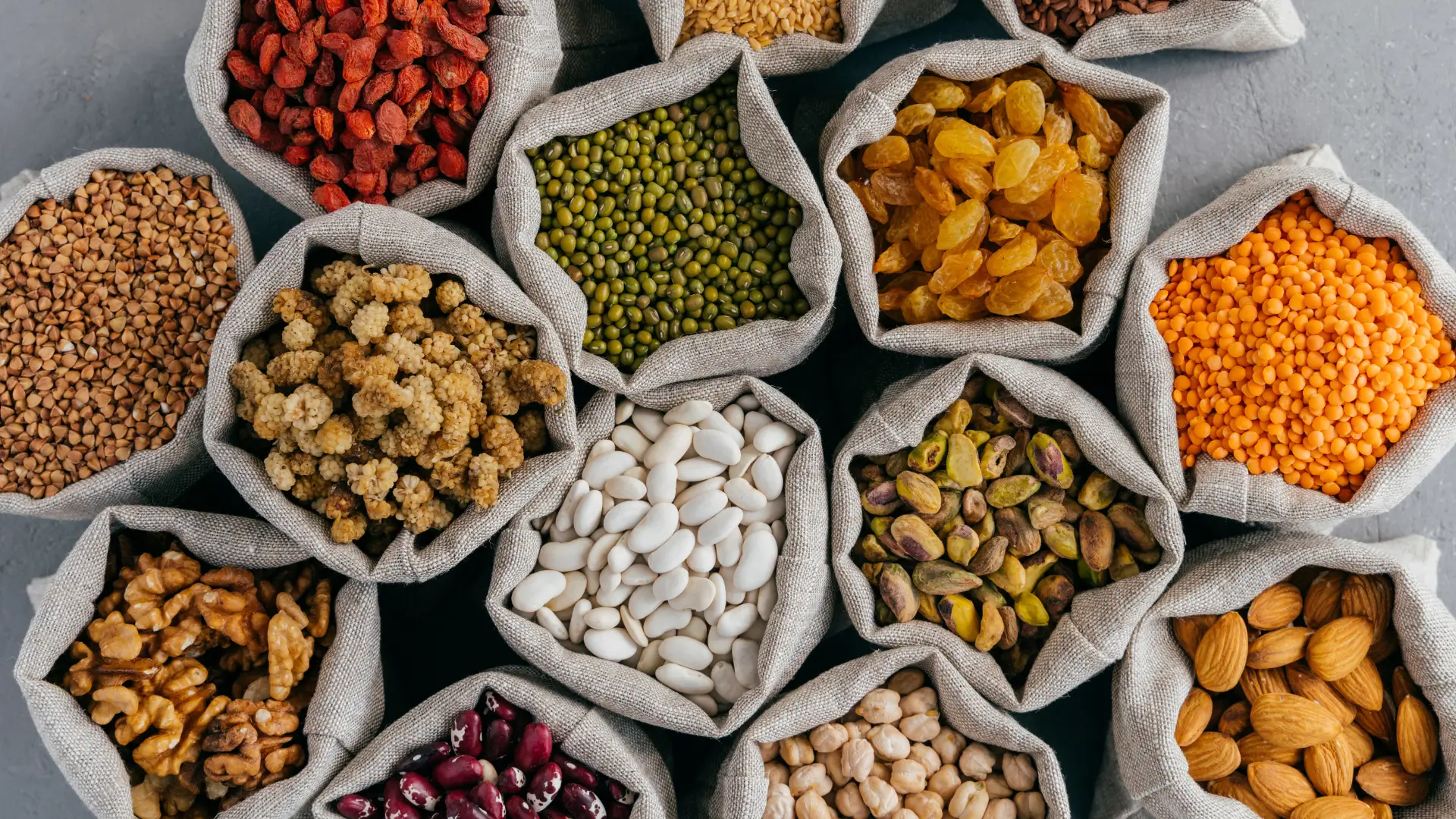 Various legumes, nuts, and dried fruits in open cloth bags
