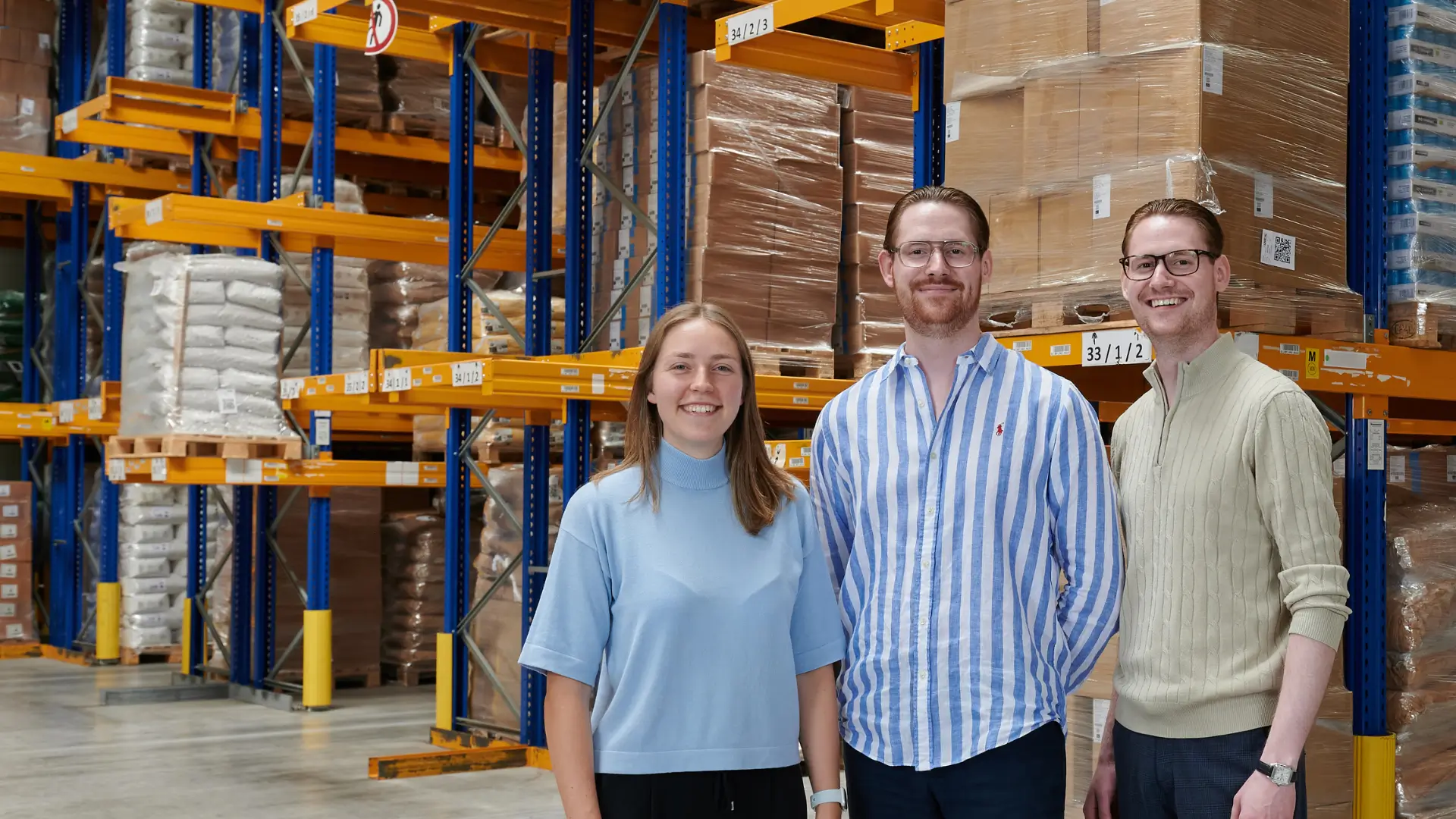 Sofie Siefert, Benjamin Bode and Daniel Bode in the warehouse in front of a fully stocked high-bay rack